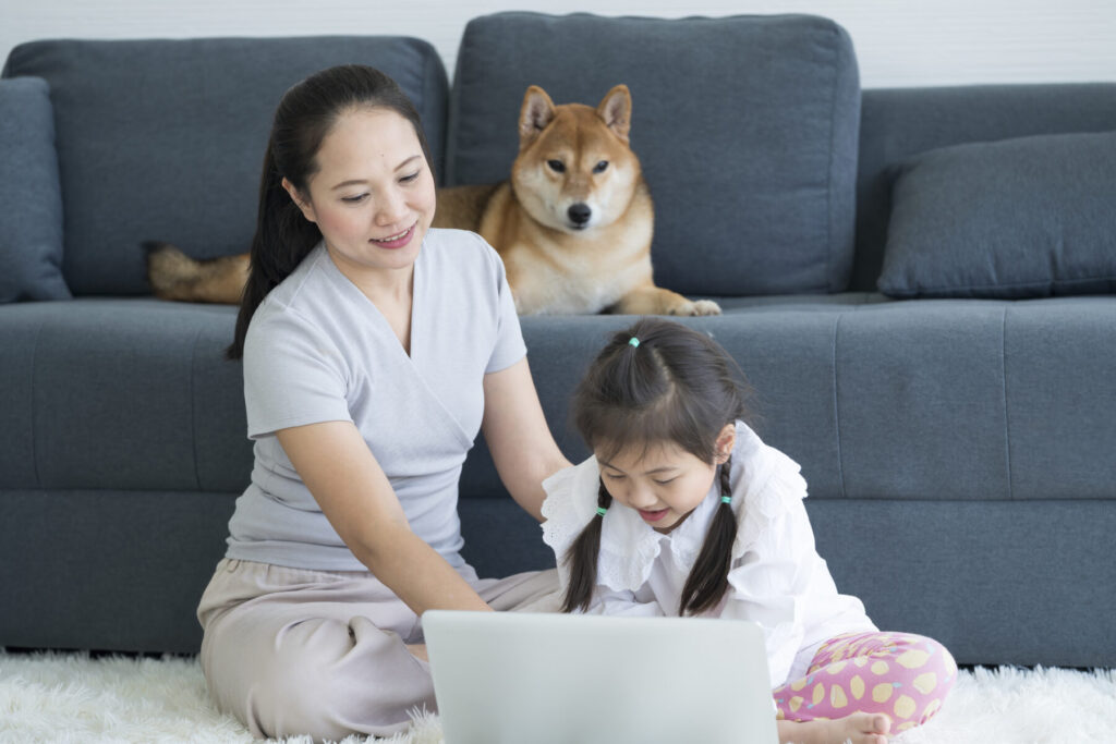 Mother and daughter on living room carpet with a dog sitting on the sofa.